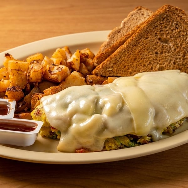A breakfast platter with a cheese-covered omelet, home fries, two slices of toast, and two ketchup cups.