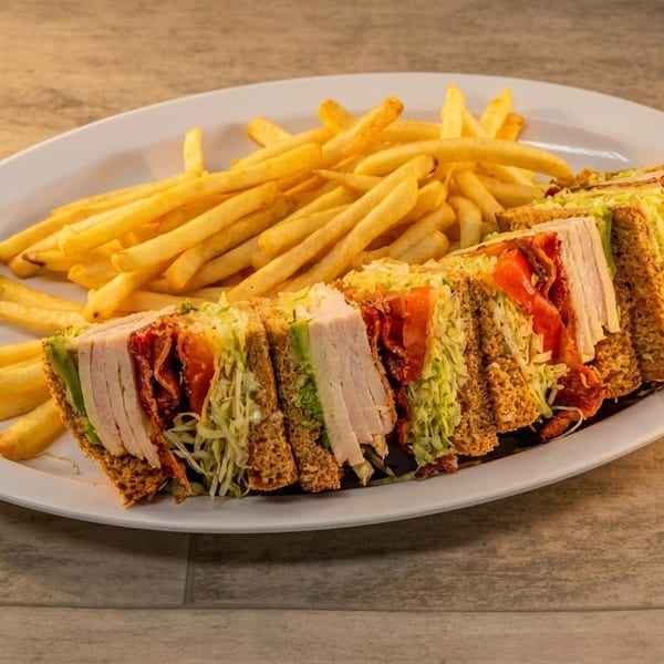 A club sandwich with turkey, bacon, lettuce, and tomato, served with a side of golden fries.