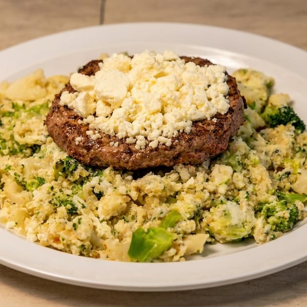 Grilled burger patty topped with crumbled feta cheese, served over a bed of cauliflower and broccoli.