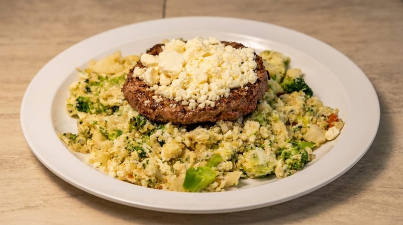 Grilled burger patty topped with crumbled feta cheese, served over a bed of cauliflower and broccoli.